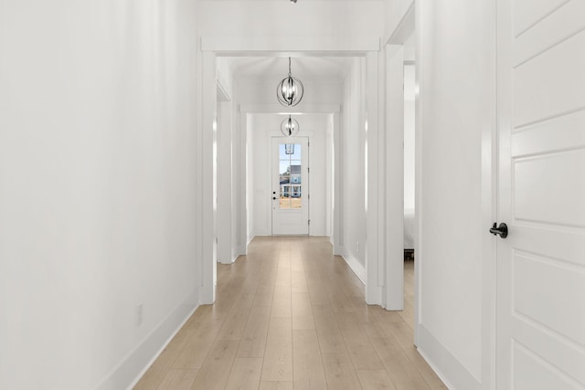 hallway with a notable chandelier, light wood-style flooring, and baseboards