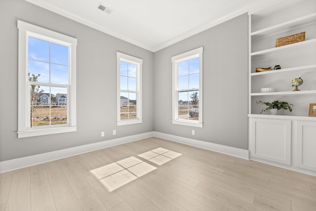 spare room with light wood finished floors, baseboards, visible vents, and ornamental molding