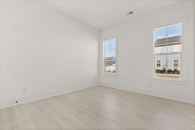 empty room with baseboards, visible vents, and light wood finished floors