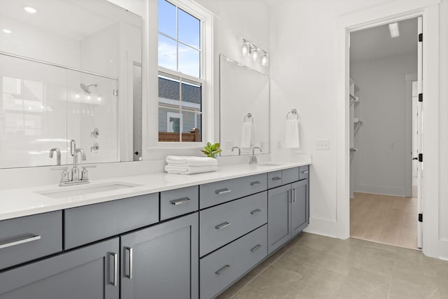 full bathroom featuring double vanity, a stall shower, baseboards, and a sink