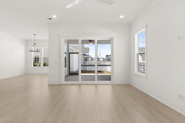 empty room featuring a healthy amount of sunlight, light wood-style flooring, and ceiling fan with notable chandelier