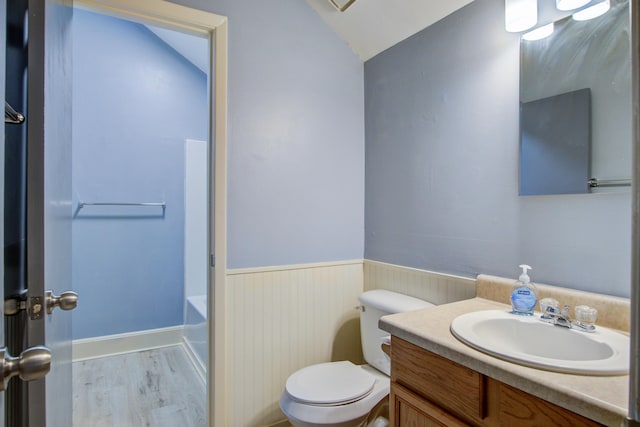 bathroom with wood-type flooring, lofted ceiling, a bathtub, vanity, and toilet