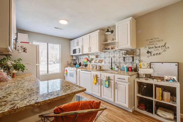 kitchen featuring light stone counters, sink, white appliances, and white cabinets