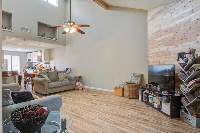 living room featuring beamed ceiling, light hardwood / wood-style floors, ceiling fan, and a high ceiling