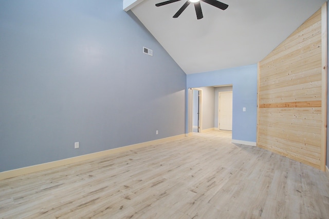 empty room featuring ceiling fan, high vaulted ceiling, light hardwood / wood-style floors, and wood walls