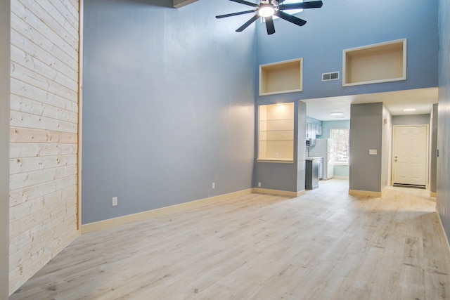 unfurnished living room featuring ceiling fan, a towering ceiling, and light hardwood / wood-style floors