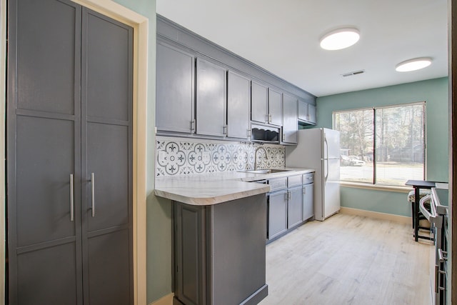 kitchen with sink, light hardwood / wood-style flooring, gray cabinetry, tasteful backsplash, and white fridge