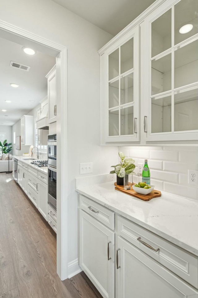 kitchen featuring visible vents, white cabinets, dark wood-style floors, glass insert cabinets, and light stone counters