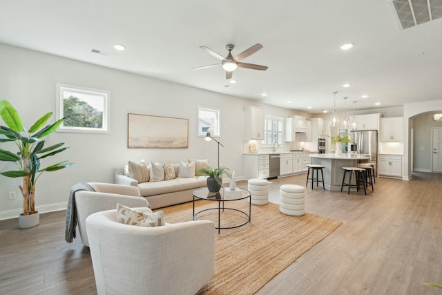 living room with light wood-style floors, arched walkways, visible vents, and recessed lighting