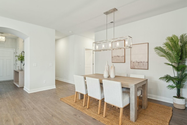 dining room with arched walkways, visible vents, baseboards, and wood finished floors