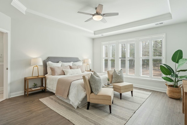 bedroom with a tray ceiling, visible vents, baseboards, and wood finished floors