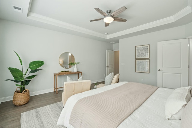 bedroom with a raised ceiling, visible vents, ornamental molding, wood finished floors, and baseboards