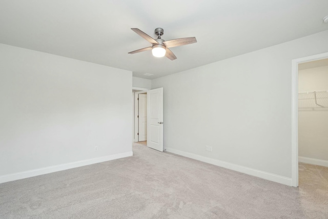 unfurnished bedroom featuring light carpet, a ceiling fan, baseboards, a spacious closet, and a closet