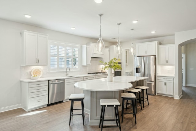 kitchen with arched walkways, appliances with stainless steel finishes, a kitchen breakfast bar, a center island, and a sink