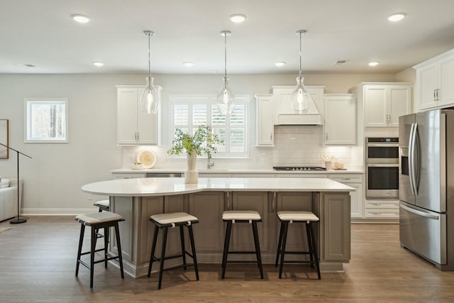 kitchen with custom exhaust hood, light countertops, appliances with stainless steel finishes, white cabinets, and a kitchen breakfast bar