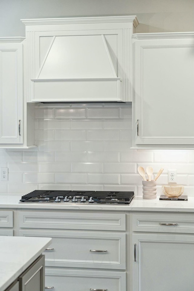 kitchen with custom exhaust hood, light countertops, white cabinetry, stainless steel gas cooktop, and backsplash