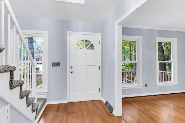 foyer entrance with ornamental molding, light hardwood / wood-style floors, a skylight, and plenty of natural light