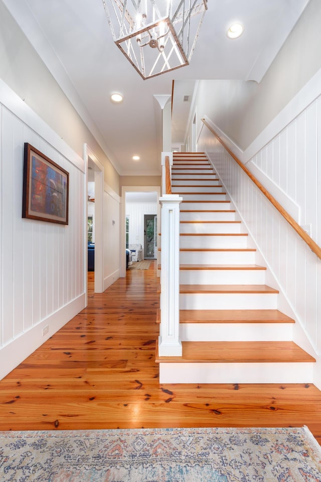 staircase featuring crown molding, a chandelier, and hardwood / wood-style flooring