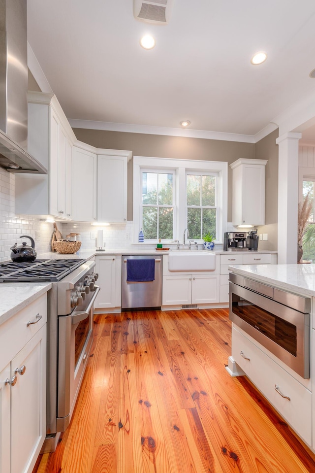 kitchen featuring white cabinetry, stainless steel appliances, range hood, and tasteful backsplash