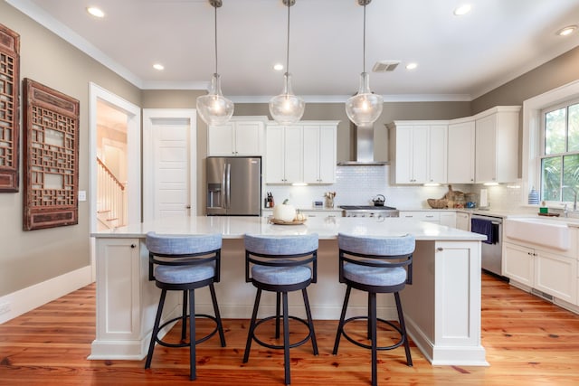 kitchen featuring stainless steel appliances, pendant lighting, a center island, and wall chimney range hood