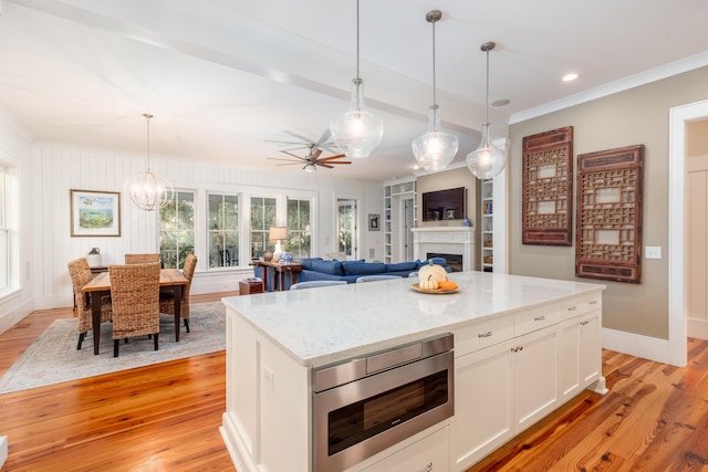 kitchen with white cabinetry, hanging light fixtures, stainless steel microwave, light stone counters, and light hardwood / wood-style floors