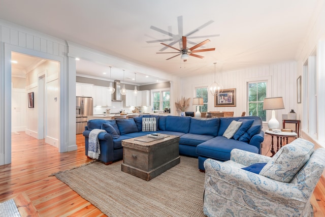 living room with ornamental molding, plenty of natural light, ceiling fan with notable chandelier, and light hardwood / wood-style floors