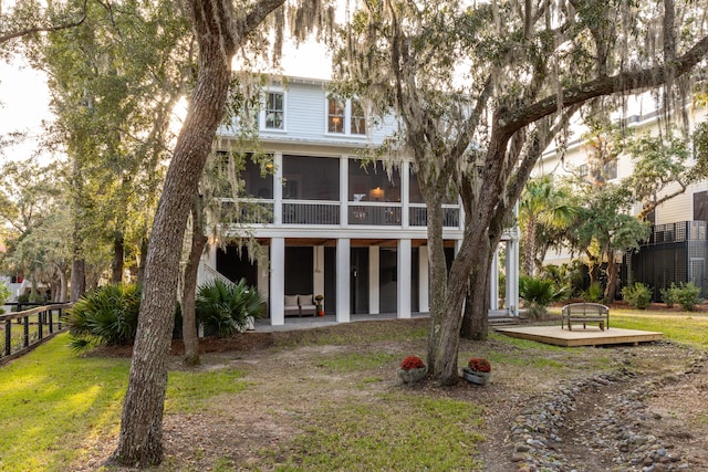 back of property with a wooden deck, a patio, a sunroom, and a lawn