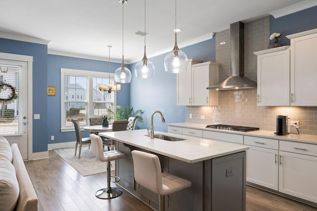 kitchen with stainless steel gas cooktop, decorative backsplash, ornamental molding, a sink, and wall chimney range hood