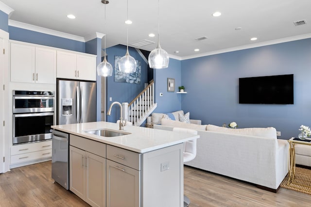 kitchen with a sink, visible vents, open floor plan, ornamental molding, and appliances with stainless steel finishes