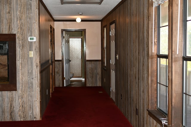 corridor featuring wood walls, ornamental molding, a textured ceiling, and dark carpet