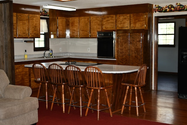 kitchen featuring black appliances, a healthy amount of sunlight, a kitchen bar, and dark wood-type flooring