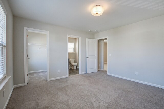 unfurnished bedroom featuring a walk in closet, ensuite bathroom, a closet, and light colored carpet