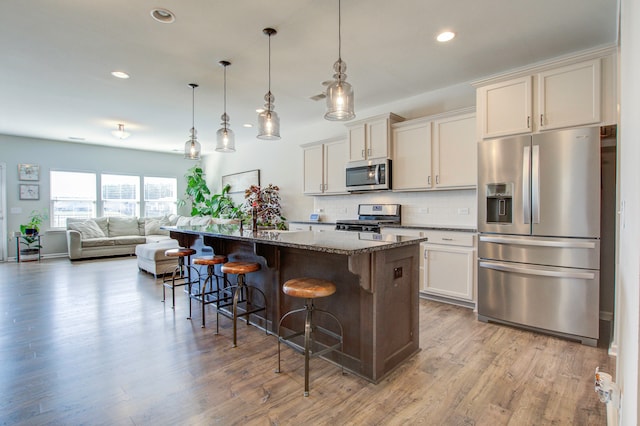 kitchen featuring a kitchen island with sink, dark stone counters, light hardwood / wood-style floors, a kitchen bar, and stainless steel appliances