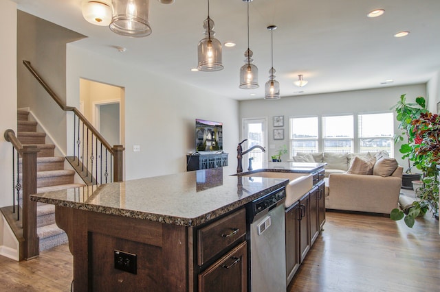 kitchen featuring dishwasher, light hardwood / wood-style flooring, light stone countertops, and a kitchen island with sink