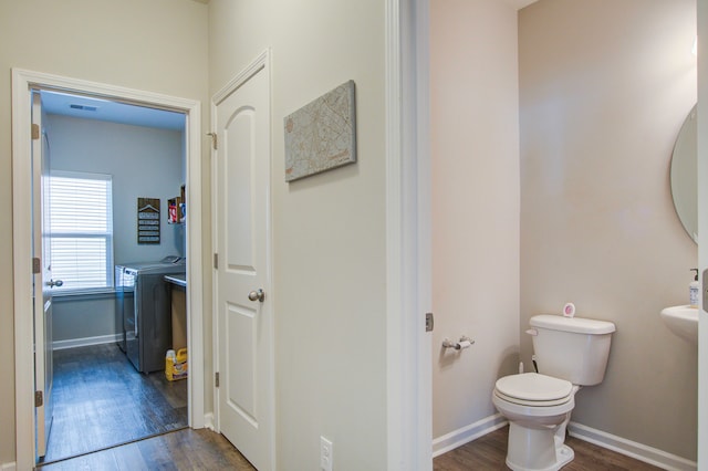 bathroom with independent washer and dryer, hardwood / wood-style flooring, and toilet