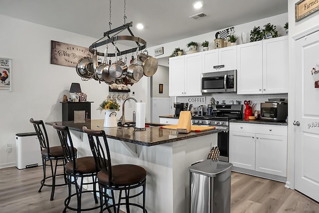 kitchen featuring backsplash, stainless steel appliances, an island with sink, and white cabinets