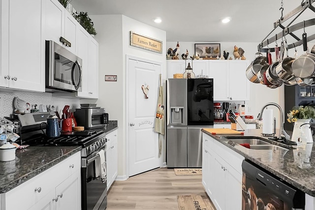 kitchen featuring appliances with stainless steel finishes, sink, dark stone countertops, and white cabinets