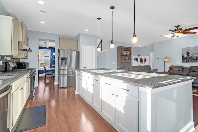 kitchen featuring dark wood-type flooring, a center island, hanging light fixtures, dark stone countertops, and appliances with stainless steel finishes