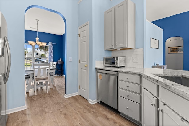 kitchen featuring backsplash, stainless steel dishwasher, white cabinetry, hanging light fixtures, and light stone countertops