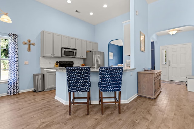 kitchen featuring backsplash, light hardwood / wood-style flooring, appliances with stainless steel finishes, gray cabinetry, and light stone counters