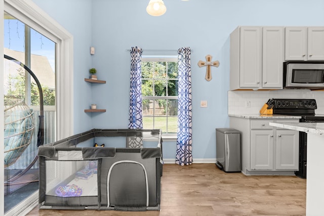 kitchen featuring tasteful backsplash, light wood-type flooring, light stone countertops, white cabinets, and black / electric stove