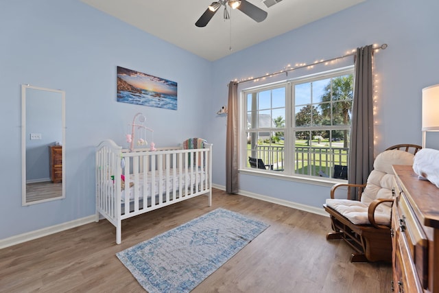 bedroom featuring ceiling fan, wood-type flooring, and a crib