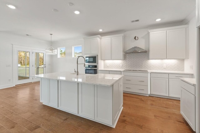 kitchen with a center island with sink, decorative light fixtures, light hardwood / wood-style floors, white cabinets, and stainless steel microwave