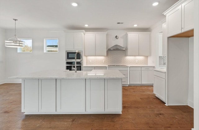 kitchen with white cabinetry, light stone counters, and a center island with sink