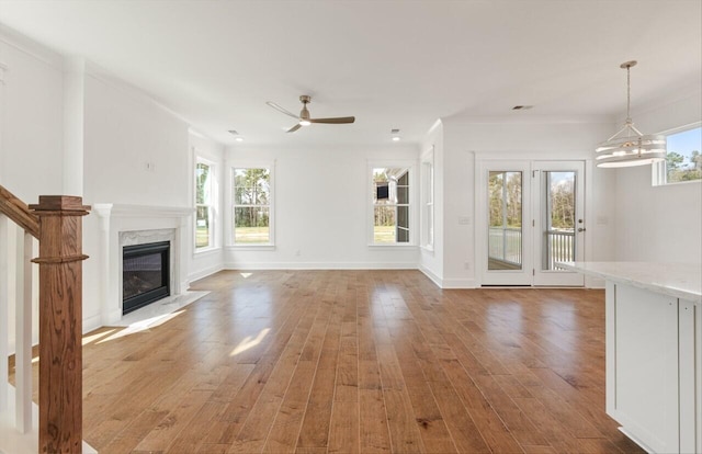 unfurnished living room featuring wood-type flooring, ceiling fan with notable chandelier, a premium fireplace, and plenty of natural light