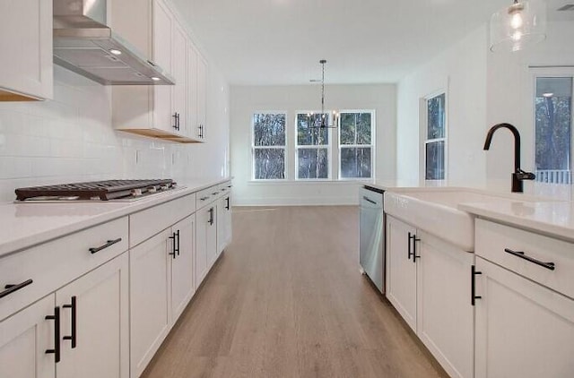 kitchen featuring wall chimney range hood, light hardwood / wood-style flooring, white cabinetry, stainless steel appliances, and decorative light fixtures