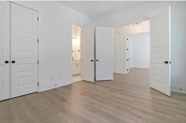 unfurnished bedroom with ensuite bath, light wood-type flooring, and a closet