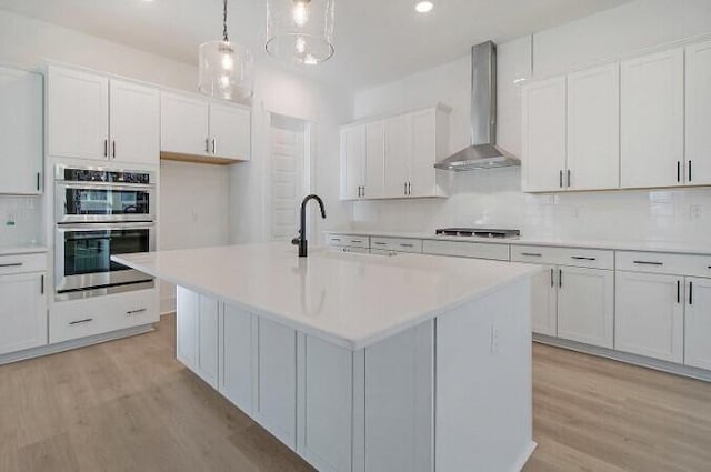 kitchen featuring hanging light fixtures, white cabinetry, a kitchen island with sink, and wall chimney exhaust hood