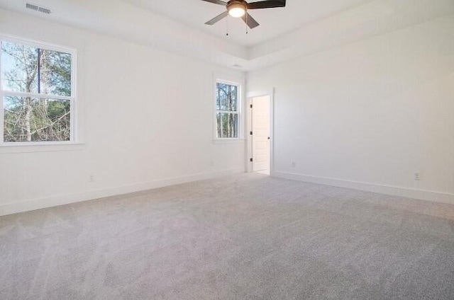 carpeted spare room featuring a tray ceiling and ceiling fan