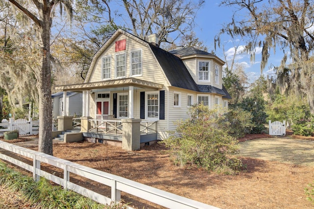 colonial inspired home featuring roof with shingles, covered porch, a gambrel roof, a gate, and fence